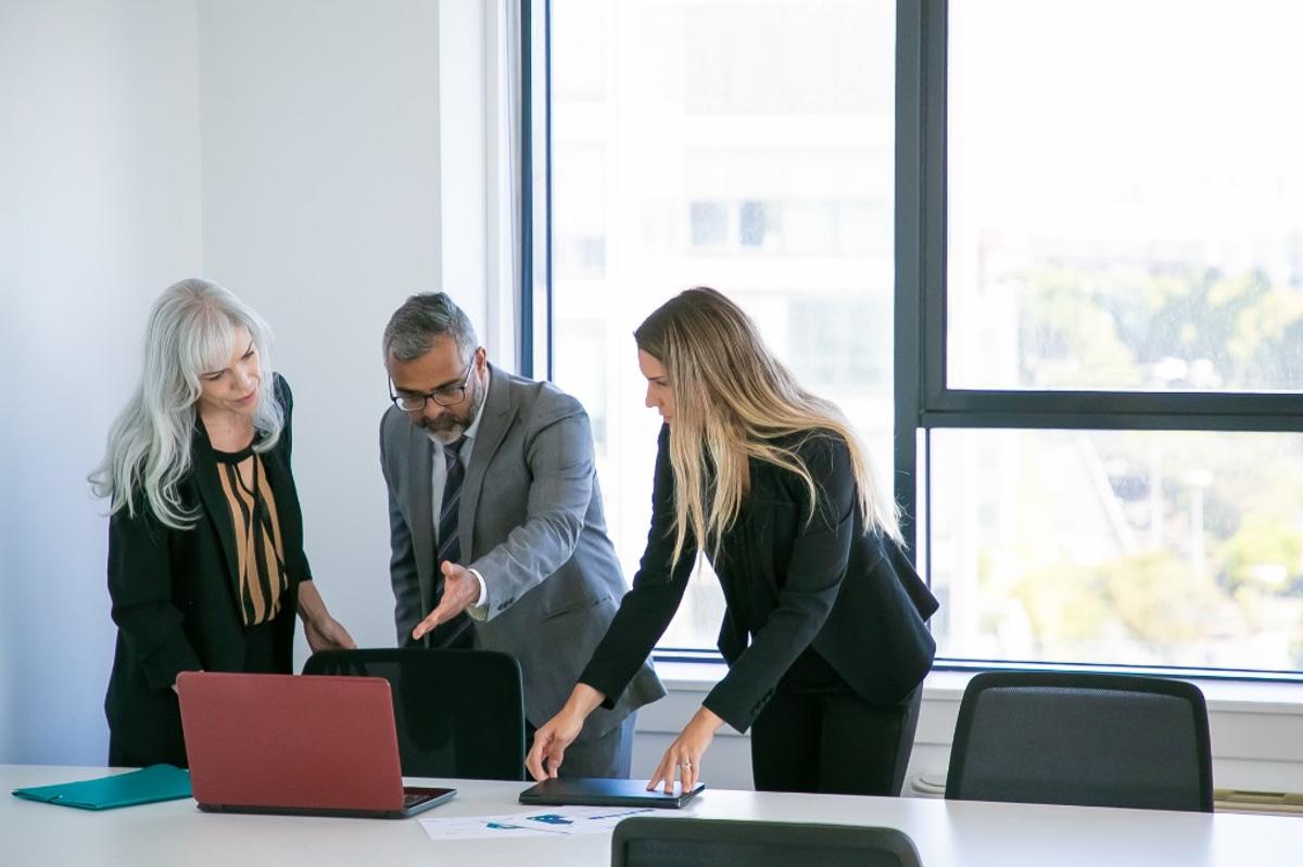 Three business professionals collaborating around a laptop and documents in a bright, modern office